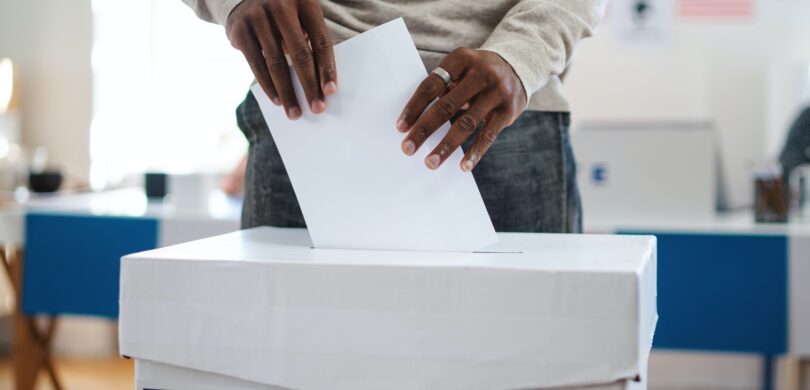 A man putting a paper ballot into a ballot box on election day.