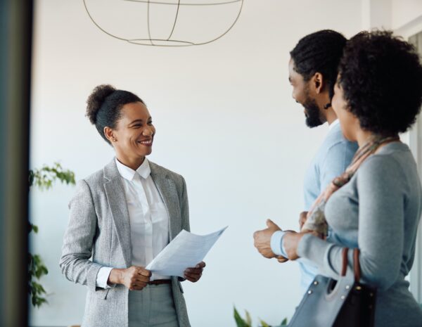 Three people stand speaking to another in an office setting.